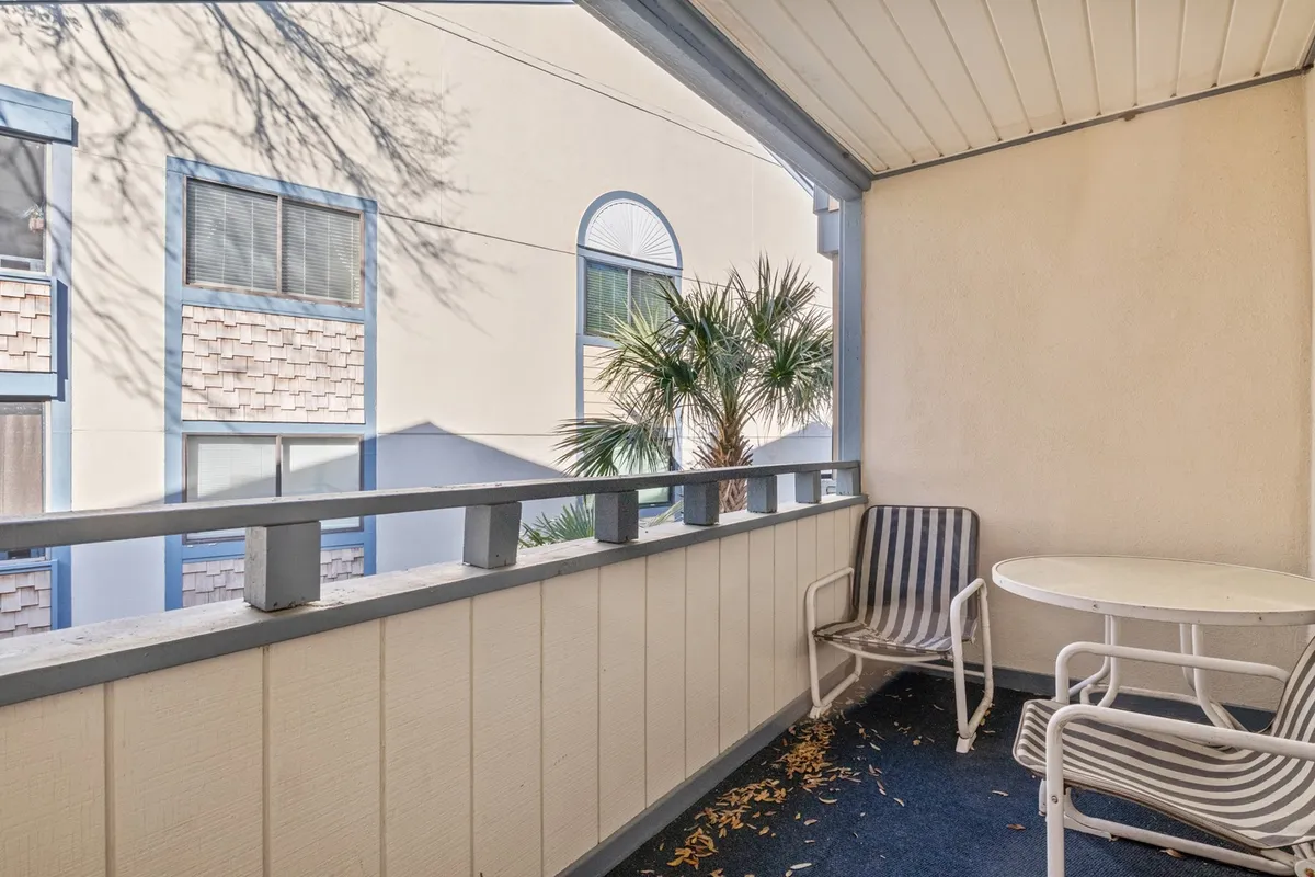 An inviting balcony scene with a table and chairs set behind a balcony railing, overlooking palm trees. The setup encourages moments of relaxation, ideal for sipping drinks or watching the sunset in the fresh coastal air.