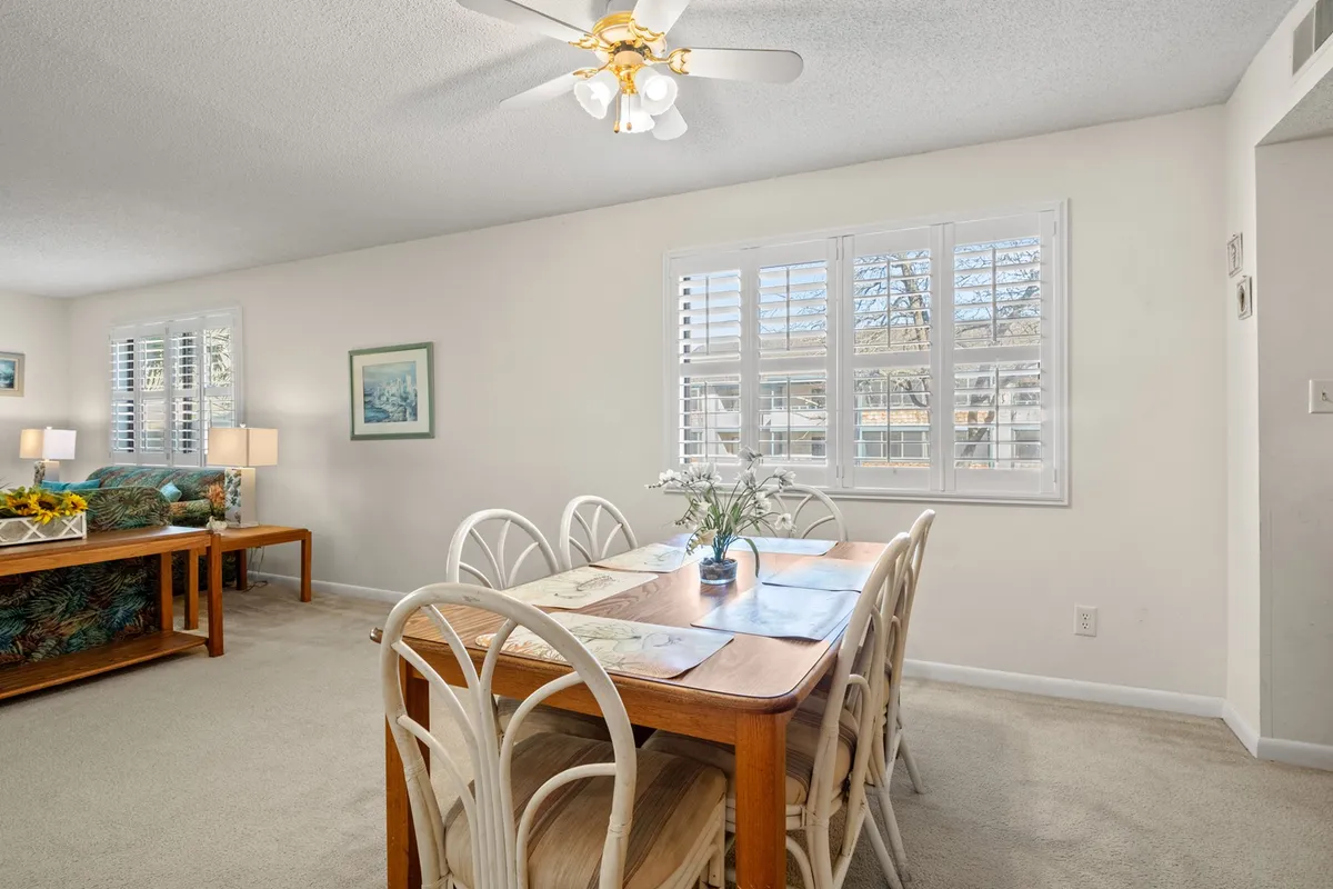A cozy dining area featuring a central dining table with several chairs, surrounded by warm decorative touches and plants. The adjacent seating area ensures a seamless flow between dining and lounging, highlighting the open-plan design.