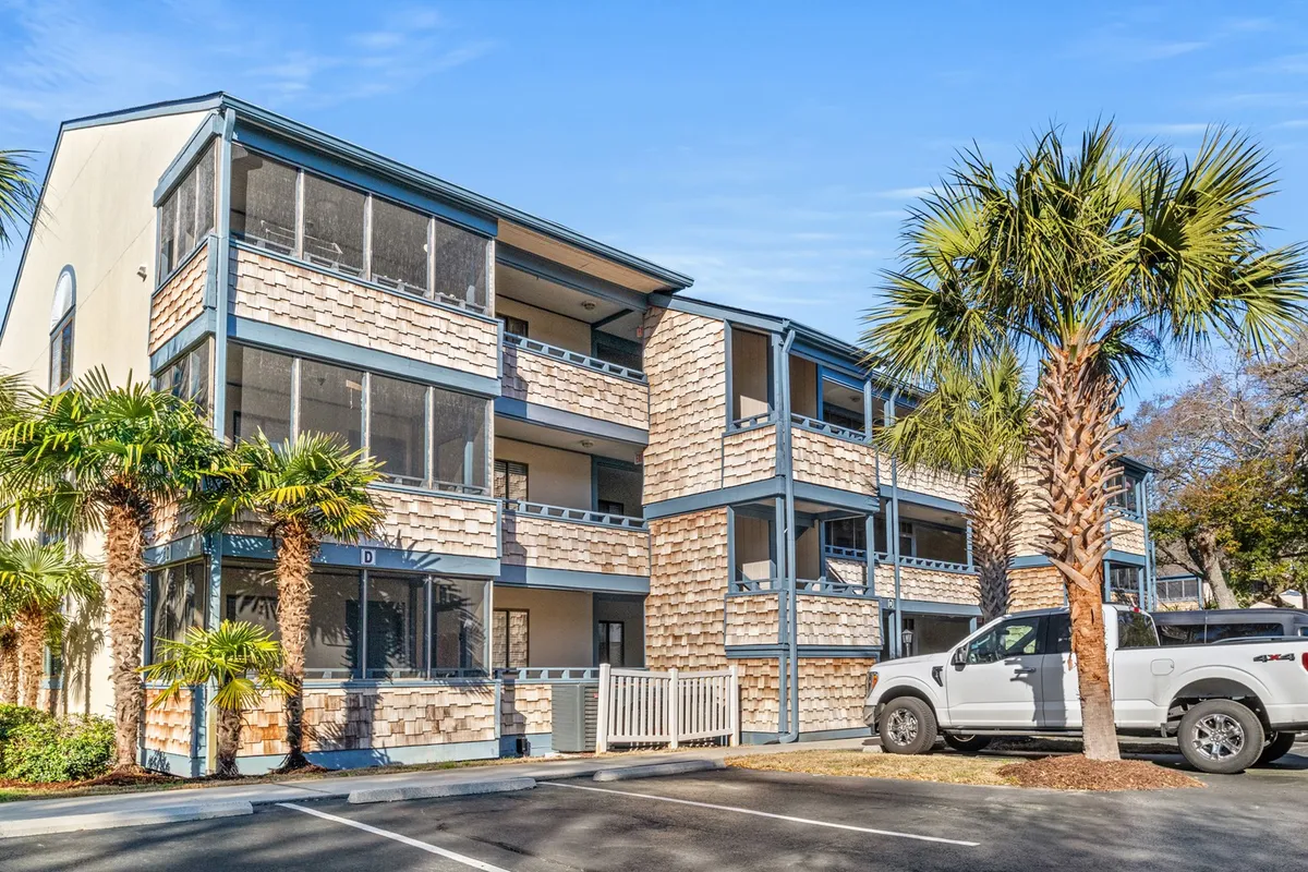 A broad exterior view of the Summertree Village building, featuring palm trees, screened balconies, and a relaxed, sunlit atmosphere. The architecture and landscaping suggest a welcoming environment ideal for group gatherings and easy access to local attractions.