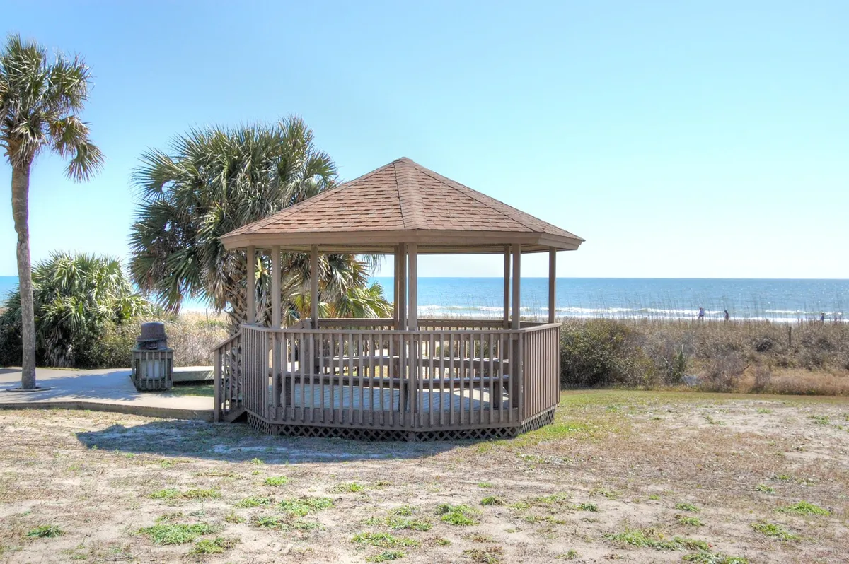 A wooden gazebo overlooks the ocean, framed by swaying palm trees. The serene setting is ideal for enjoying sunrises, gentle breezes, or quiet gatherings with friends, epitomizing the coastal lifestyle that snowbirds seek during winter stays.