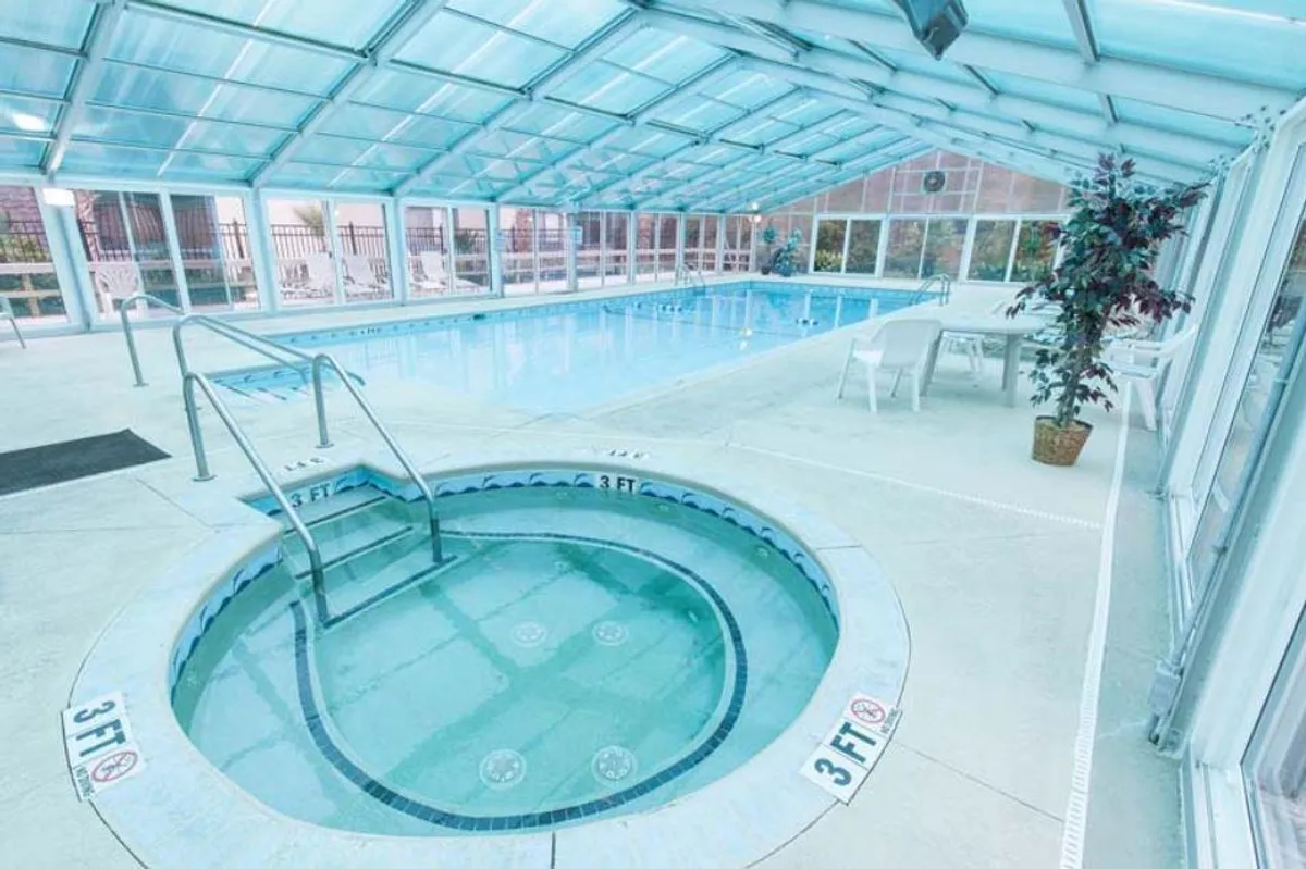 A bright and airy indoor pool area with a hot tub and comfortable seating, accented by large windows letting in natural light. The inviting space caters to both relaxation and socializing, regardless of the weather outside.