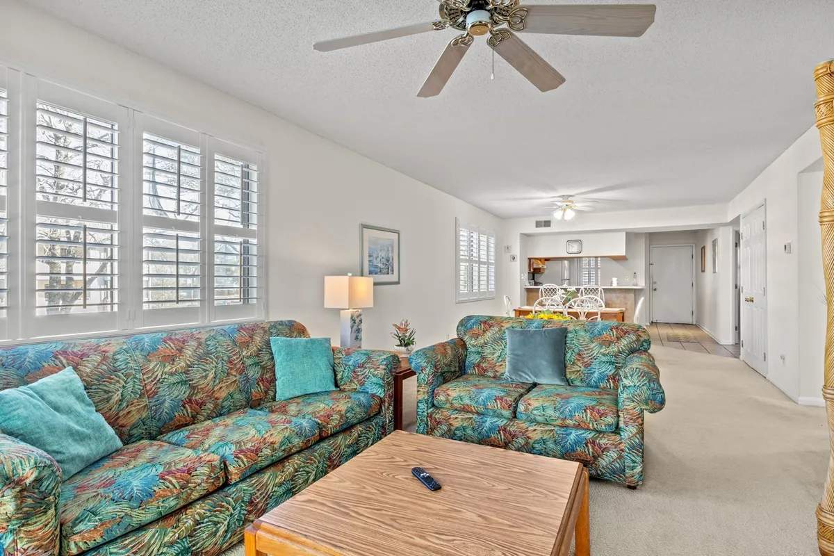 Another angle on the living area, showing colorful sofas, a wooden coffee table, a ceiling fan, and artwork on the walls. The setup feels intimate and welcoming, ideal for casual gatherings, playing games, or quiet relaxation.